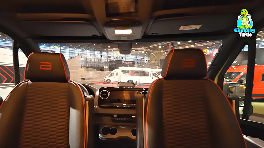 Zwei schwarze Fahrerhaussitze mit orangen Nähten und gesticktem Logo, Blick nach vorn