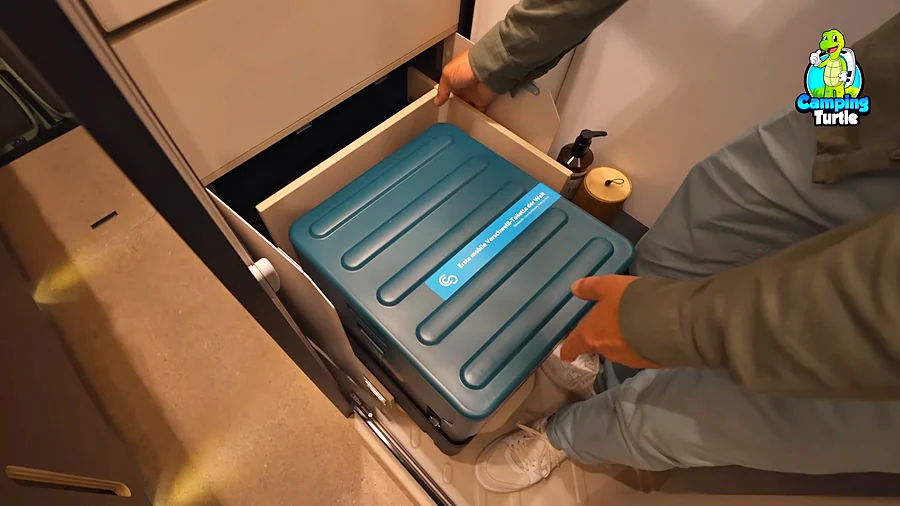 Eine Hand zieht einen Auszug mit einer petrolfarbenen Clesana-Toilette heraus