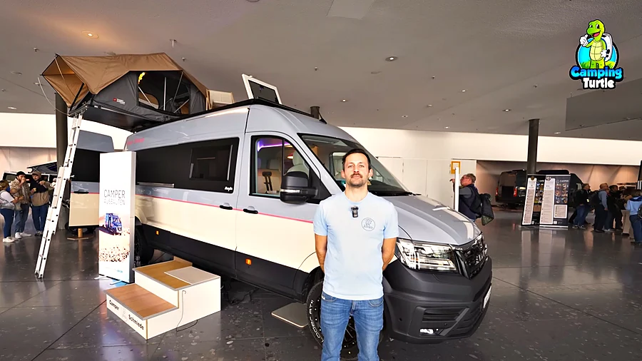 Christian Dinraths steht vor der grau-cremefarbenen Camper Schmiede Marylin mit Dachzelt auf der CMT 2025.