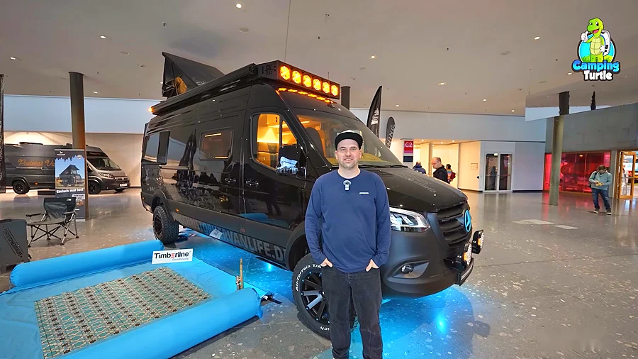 Christopher Möckel steht auf der CMT 2025 vor seinem schwarzen Mercedes Sprinter 4x4 mit Dachzelt und Zusatzscheinwerfern