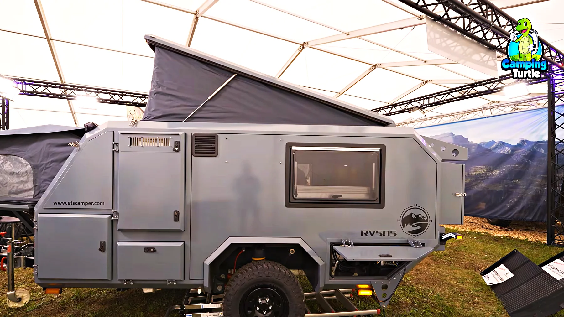 Grauer ETS Camper RV505 in der Seitenansicht mit aufgestelltem Dach und ausgeklappter Front über der Deichsel