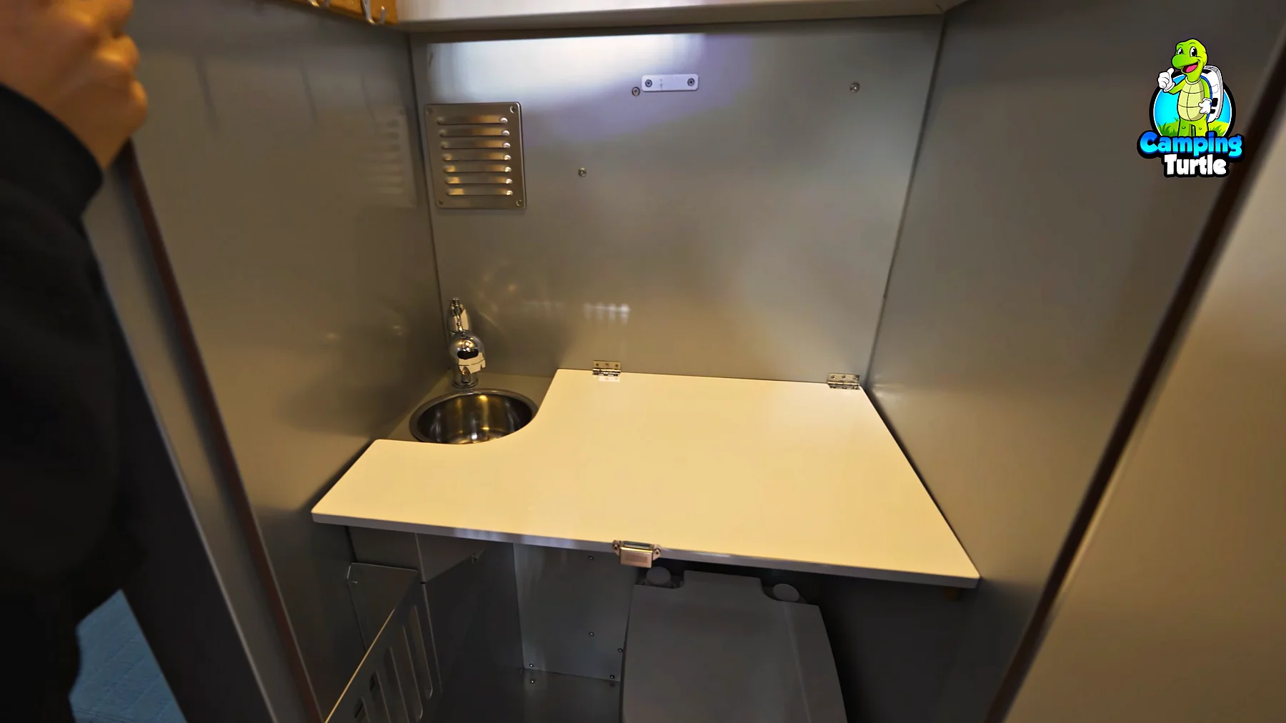 Kleines Bad mit Waschbecken und heruntergeklappter heller Platte über der Toilette