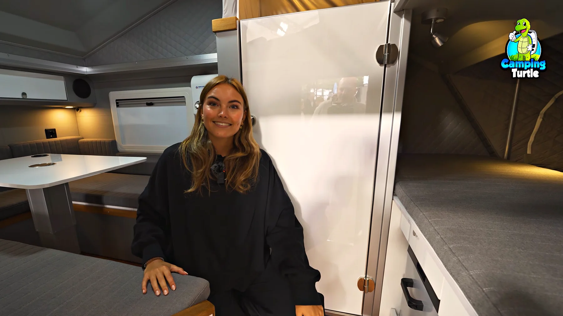 Jil sitzt in der hellen Sitzgruppe des sandfarbenen Trailers, rechts die Badtür