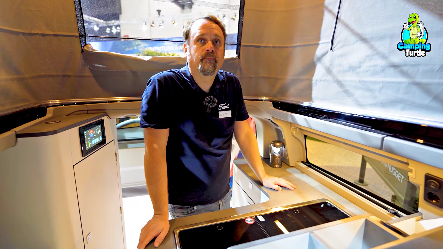 Tiemo Etzold steht unter dem aufgestellten Dach im Heck des Ford Nugget, links der Touchscreen am Schrank, vorn die Küche.