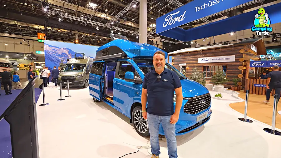 Tiemo Etzold steht vor dem blauen Ford Nugget mit Hochdach auf dem Caravan Salon 2025.