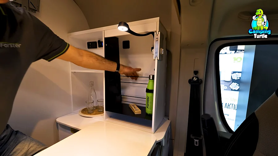Geöffneter weißer Schrank mit LED-Leuchte, Fächern und Steckdosen, davor die ausgeklappte Arbeitsplatte