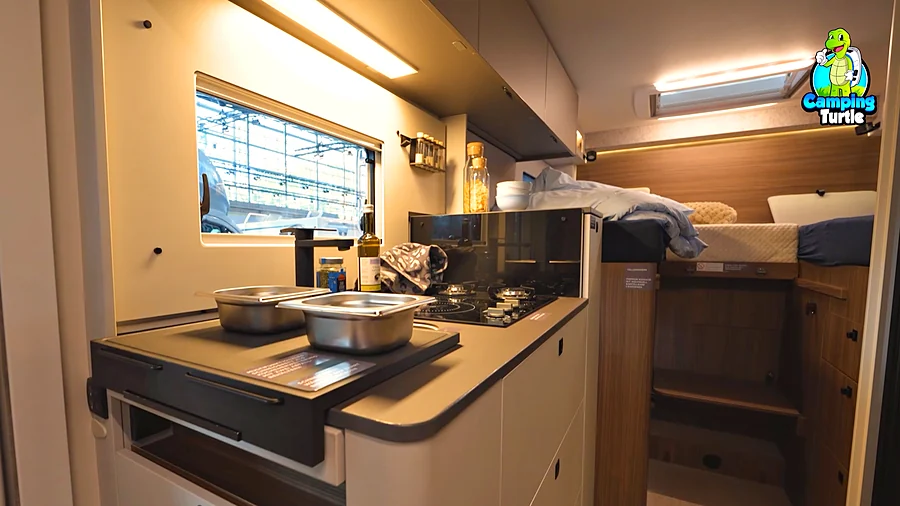 Küche des LMC Cruiser 740 EL mit Kombi-Kochfeld aus Induktionsfläche und zwei Gasflammen, davor das Frankfurter Brett mit zwei Edelstahlschalen und im Hintergrund die Längsbetten