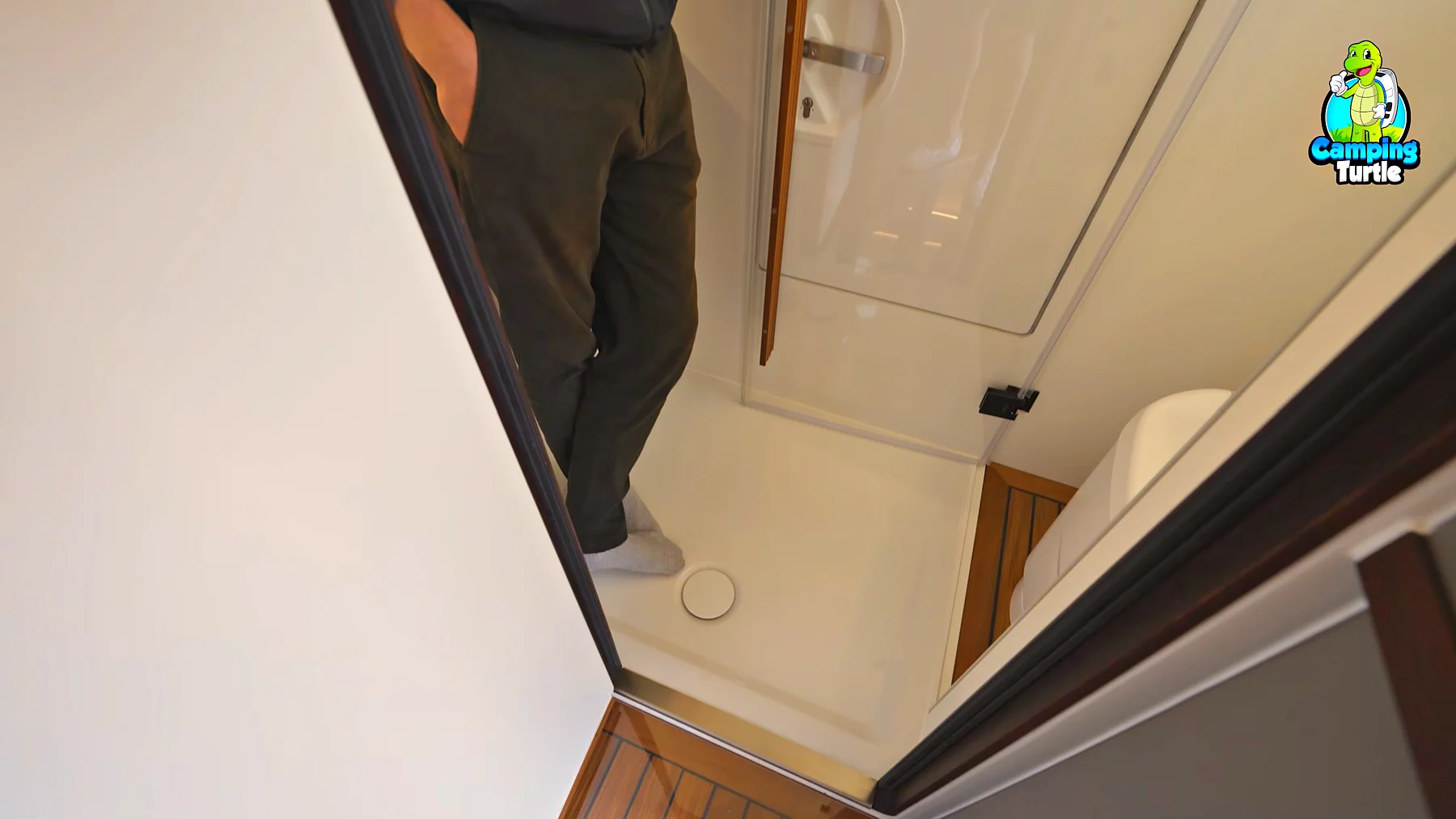 Blick ins Bad mit Duschwanne und Toilette hinter einer Acrylglastür