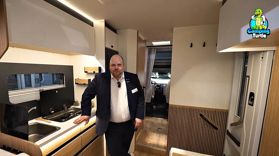 Marco Sander an der Küche des Pilote P720U mit Gaskocher, Spüle und Hängeschränken, dahinter der Flur zum Fahrerhaus