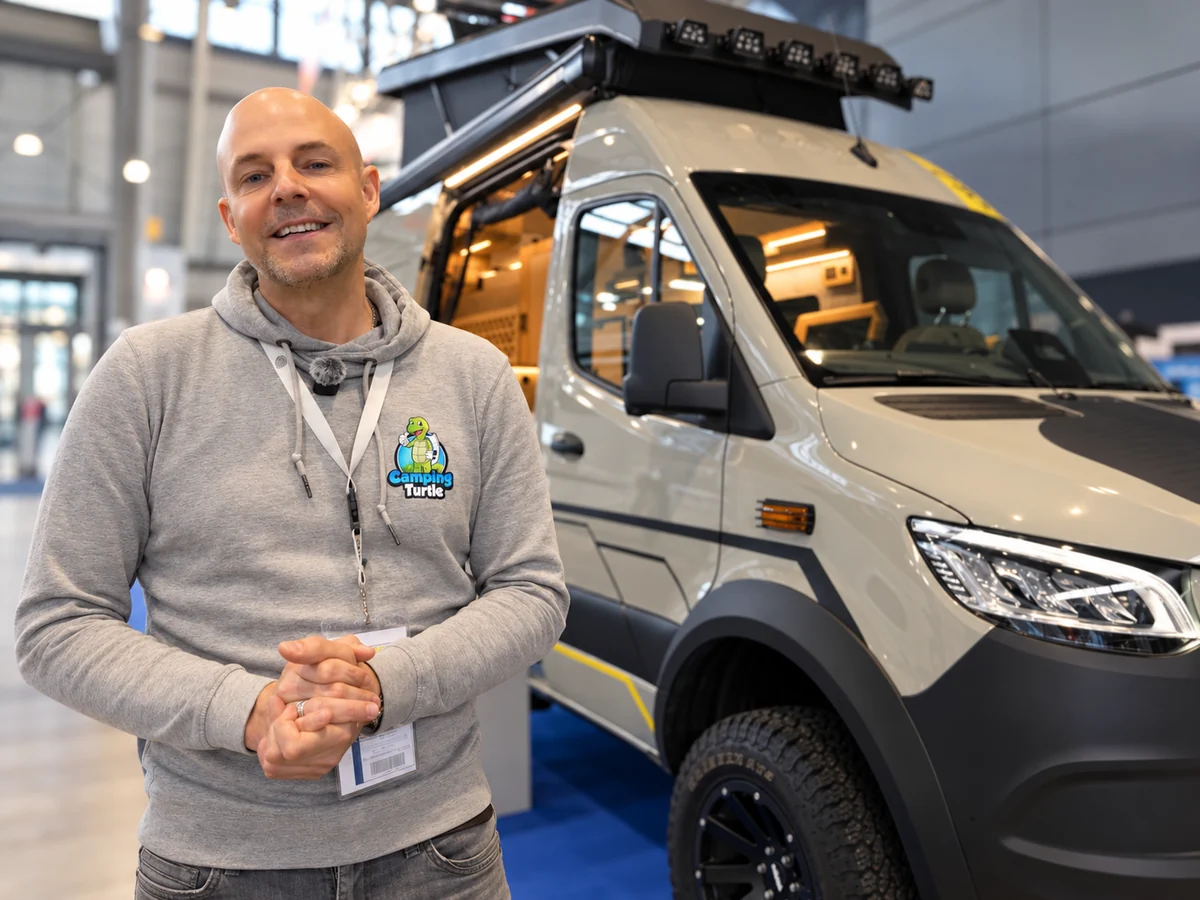 Thomas von CampingTurtle mit Mikrofon vor einem Allrad-Kastenwagen auf einer Messe