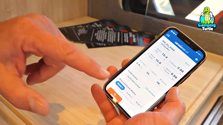 Smartphone mit der App der CARAWATER-Pumpe, die Spannung, Wasserdruck und entnommene Liter anzeigt