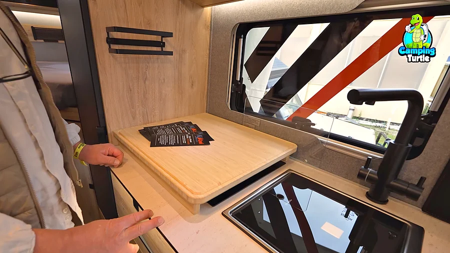 Schneidebrett aus Bambus über dem Kochfeld in der Küche des Eura Mobil Xtura Xplorer, daneben Spüle und schwarze Armatur